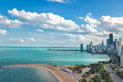 Aerial view of Chicago skyline with Lake Michigan, sandy beaches, and downtown skyscrapers under blue sky with white clouds