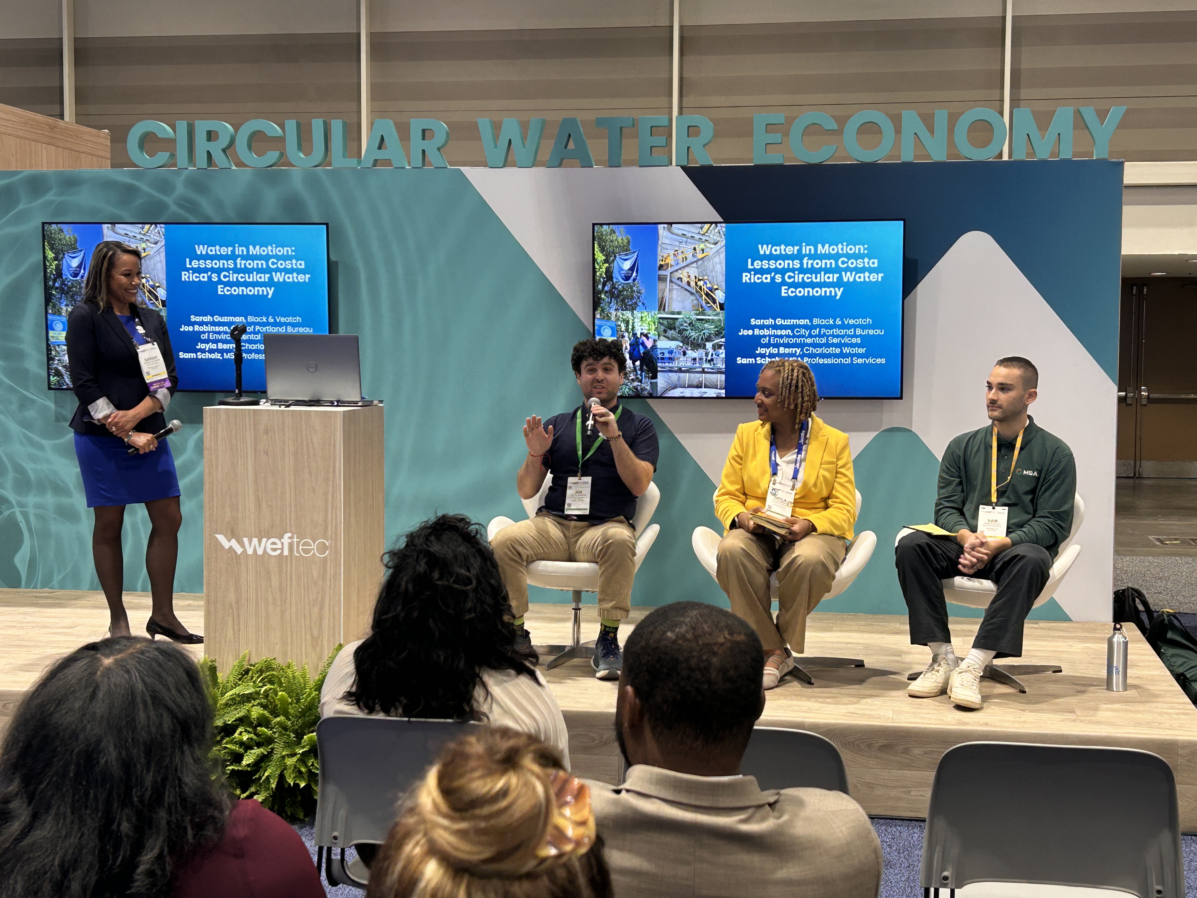 Panel discussion on circular water economy at conference with four speakers and audience members seated in front of branded backdrop.