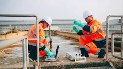 Two workers in safety gear performing water quality testing at an industrial treatment facility