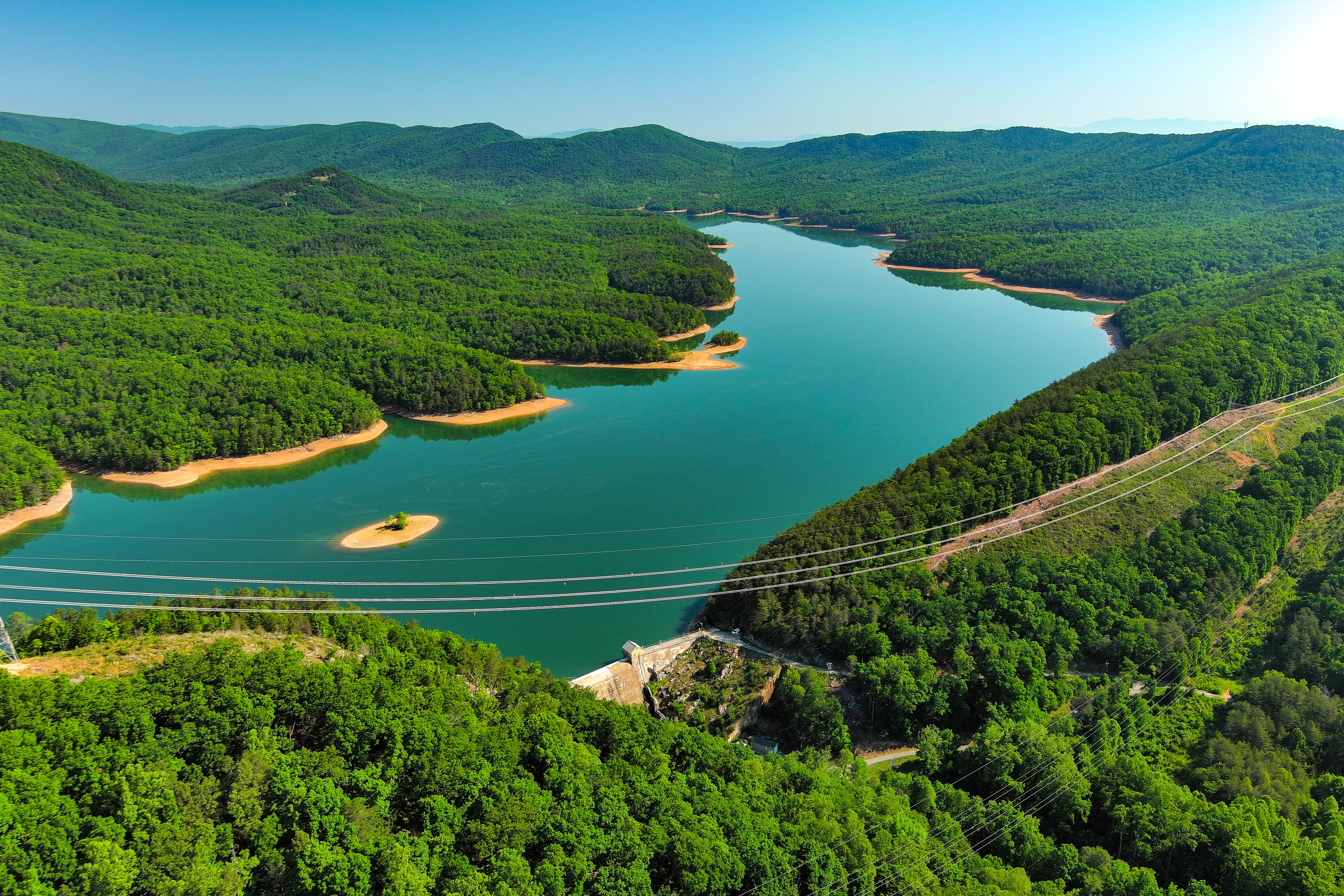Aerial view of turquoise reservoir surrounded by dense green forest and mountains with a bridge crossing the water