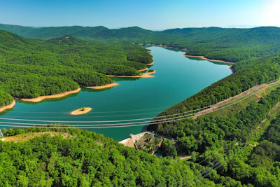 Aerial view of turquoise reservoir surrounded by dense green forest and mountains with a bridge crossing the water