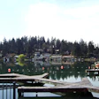 Waterfront homes and docks reflected in calm lake water surrounded by evergreen forest