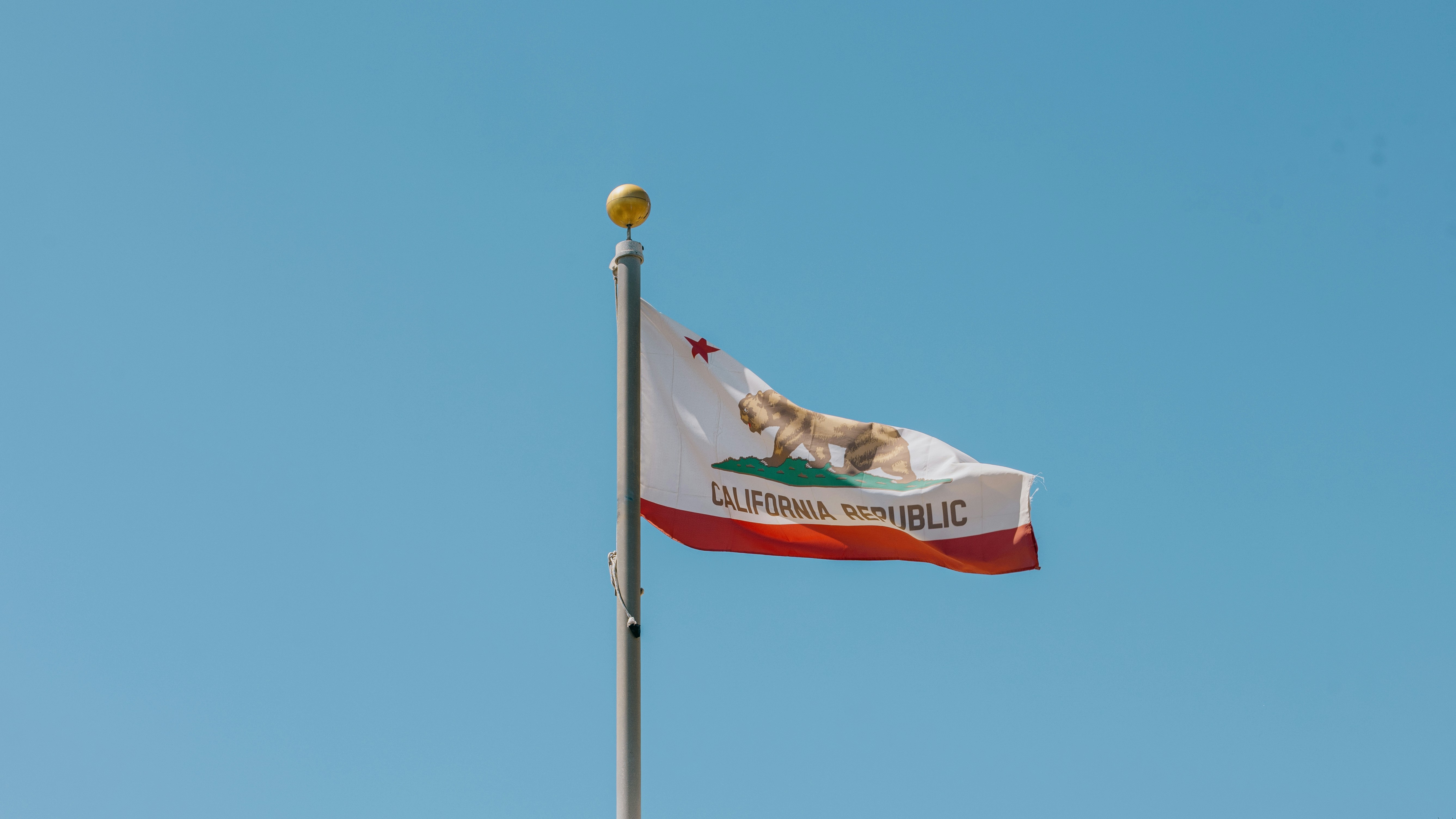 California state flag waving on a flagpole against a clear blue sky