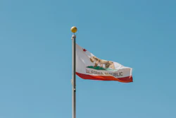 California state flag waving on a flagpole against a clear blue sky