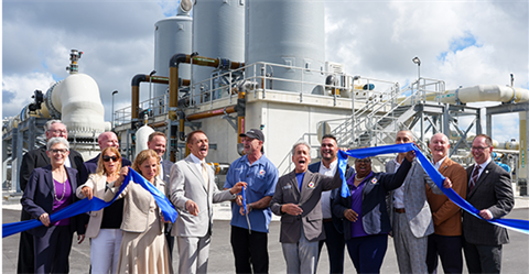 Group of business professionals cutting blue ribbon at industrial facility opening ceremony