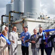 Group of business professionals cutting blue ribbon at industrial facility opening ceremony