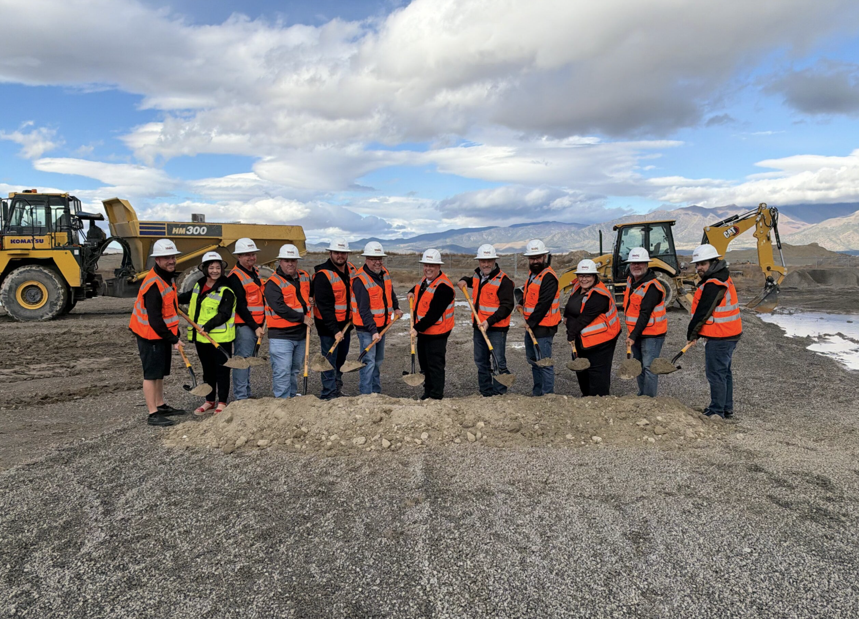 Construction crew wearing orange safety vests and hard hats standing in front of heavy machinery at a mining or quarry site.